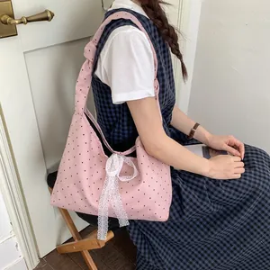 Pink polka dot canvas tote bag with white lace bow detail worn by a model