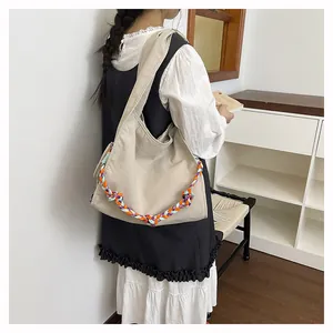 Borsa hobo in tela beige con tracolla intrecciata colorata indossata sulla spalla