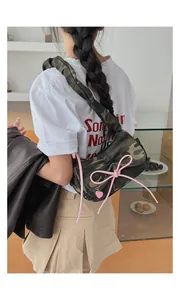 Close-up of camo shoulder bag featuring pink bow detailing and heart charm on a model