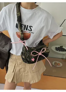 Close-up of camo canvas baguette bag with pink bow ribbon and heart charm detail