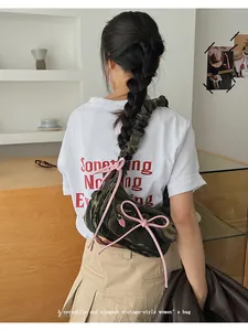Close-up of camouflage baguette bag with pink bow detail worn by a model on shoulder
