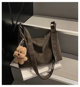Detail of a brown matte leather tote bag with a plush bear charm and gold logo lettering