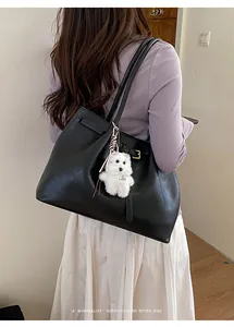 Detail einer schwarzen Leder-Tote-Bag mit süßem weißem Plüschwelpen-Anhänger und Schnalle