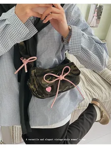 Detail of camouflage canvas bag featuring a pink bow and a heart-shaped pendant charm