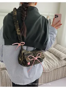 Detail of camouflage baguette bag featuring a pink bow decoration and heart charm