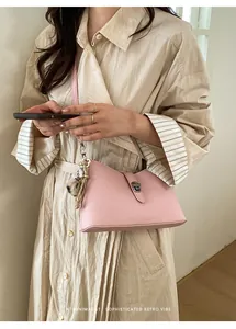 Detail of pink lychee leather handbag with decorative pom-pom and metallic charm