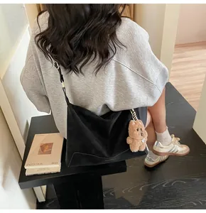 Detail of matte black crossbody bag with wide strap and cute brown bear pendant charm