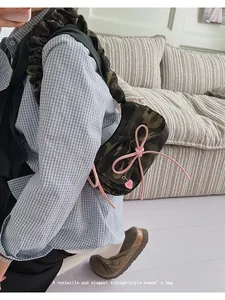 Detail of pink bow and heart pendant on camouflage baguette bag with ruffled strap
