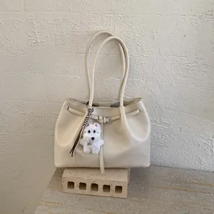 Minimalistische beige Leder-Tote-Bag mit Plüschwelpen-Anhänger auf Steinsockel