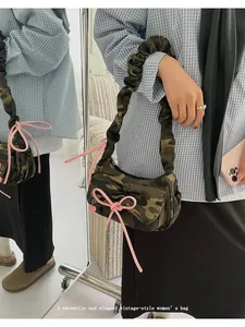 Detail of camo shoulder bag featuring pink bow accents and ruched strap in mirror view