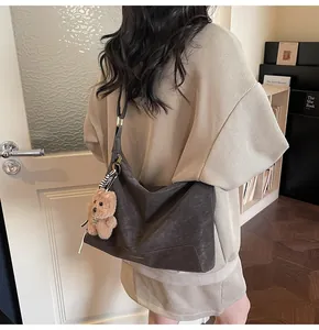 Detail of grey frosted leather crossbody bag with a plush bear charm and adjustable strap