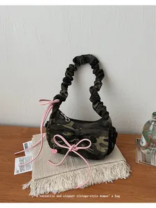 Detailed view of camouflage baguette bag with pink bow ribbon and heart charm accent