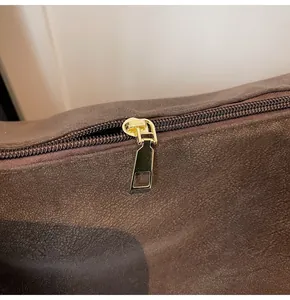 Detailed close-up of dark brown matte leather texture and golden metal zipper hardware