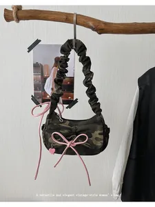 Close-up of camouflage baguette bag featuring pink bows and a ruched cloud strap