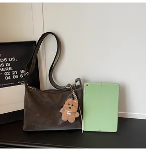 Detail of dark brown vintage crossbody bag with soft texture and cute bear pendant