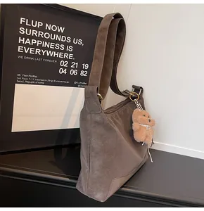 Detailed close-up of a dark brown frosted suede shoulder bag with a plush bear charm