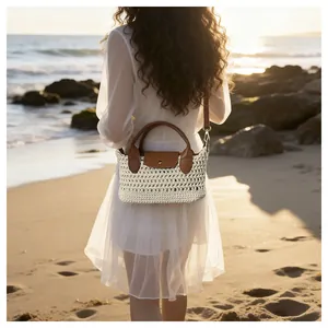 Detail van een geweven crossbodytas met leren handvatten op het strand bij zonsondergang