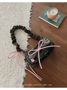 Detail of camouflage baguette bag with pink bow, heart charm and ruched handle