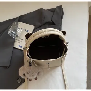 Vista macro della borsa a secchiello crema con pelle a grana, chiusura magnetica e ciondolo
