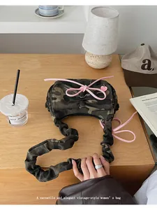 Detailed view of camouflage baguette bag with pink bow accent and pleated shoulder strap