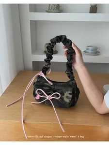 Detailed view of camouflage baguette bag featuring pink bows and a heart charm