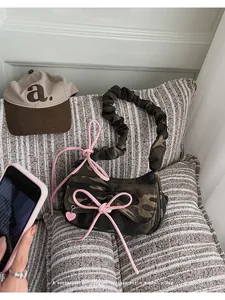 Detail of vintage camo handbag with pink bows and heart charm on a striped pillow