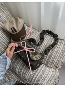 Close-up of camouflage baguette bag featuring pink bow accents and ruched shoulder strap