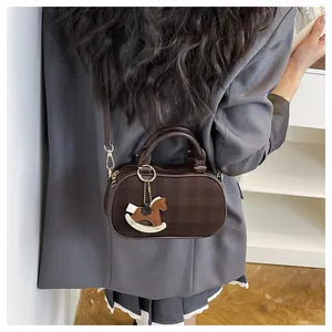 Detalle de mini bolso Boston marrón oscuro con colgante de caballo y blazer gris-azul