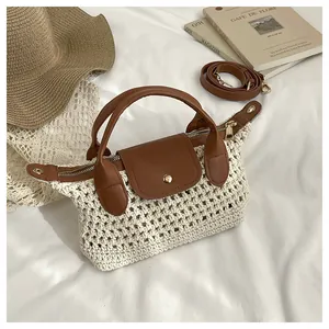 Detail van geweven strohandtas met bruine leren bies, gouden hardware en lange riem