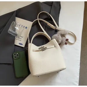 Dettaglio della borsa in pelle crema con chiusura rotante in metallo e ciondolo peluche