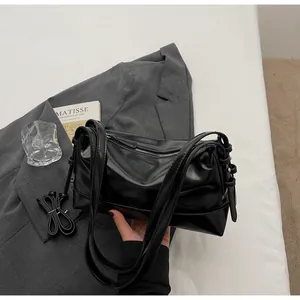 Detail shot of a black glossy PU leather underarm bag on a gray suit jacket with books