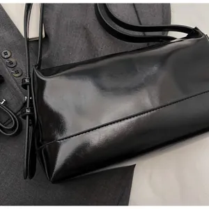 Close-up of a glossy black minimalist underarm bag with refined stitching and metallic buckles