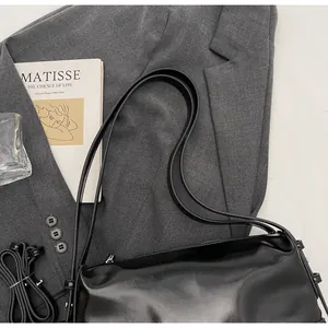 Detail shot of a black glossy pillow bag with slim straps on a grey blazer suit