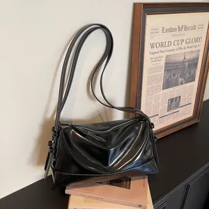 Minimalist black glossy leather pillow bag with silver zipper in a retro interior setting
