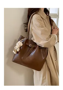 Detail of a large brown tote bag with decorative strap and cute plush bear charm