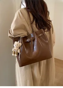 Detailed view of dark brown leather tote bag with stylish belt buckle and plush bear charm