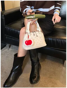 Detail der weißen Polka-Dot-Tasche mit rotem Plüsch-Anhänger auf schwarzem Ledersofa