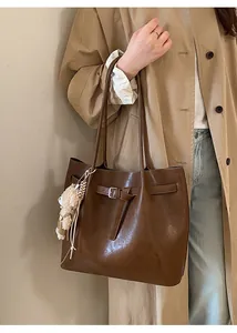 Close-up of brown faux leather tote bag with a plush bear charm on a trench coat model