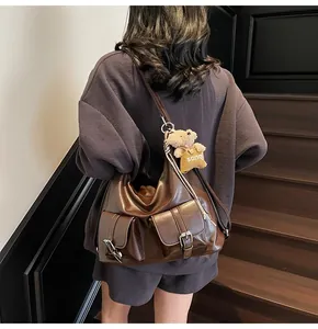 Detail einer dunkelbraunen Hobo-Tasche aus Kunstleder mit Taschen und Bärenanhänger