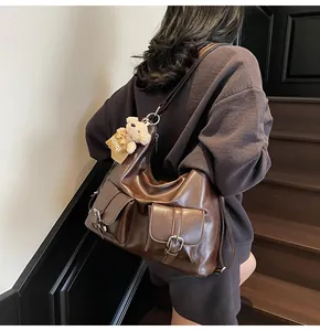 Detail einer großen braunen Kunstledertasche mit Schnallentaschen und einem Plüschbär-Anhänger