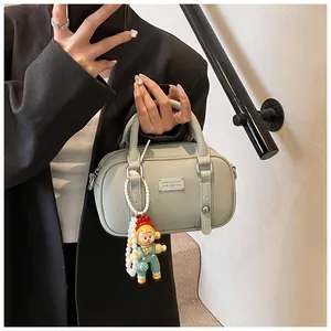 Detail van saliegroene leren tas met logoplaatje en een schattige cartoon poppenhanger
