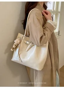 Detail of cream tote bag with metallic buckle and plush bear charm on coat sleeve