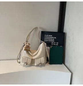 Detailansicht einer cremefarbenen Hobo-Tasche mit Silberschnallen und Bärenanhänger