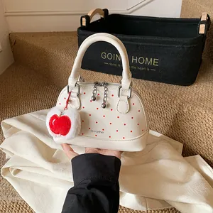 Schicke Muschel-Handtasche mit Punkten, rotem Apfelanhänger und Silberbeschlägen