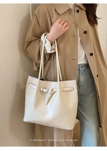 Minimalist cream tote bag with decorative buckle shown in a lifestyle commuting scene