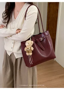 Detail of burgundy glossy tote bag featuring a decorative buckle and plush bear charm