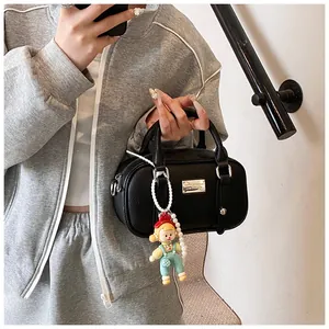 Detail van zwarte handtas met lychee-korrel, parelketting en schattige cartoon hanger