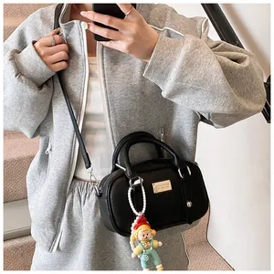 Detail van zwarte mini Boston tas met lychee textuur, zilveren logo en cartoon hanger