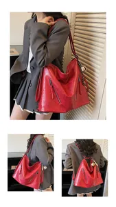 Detail view of large red vintage leather tote bag with decorative zippers and baseball charm