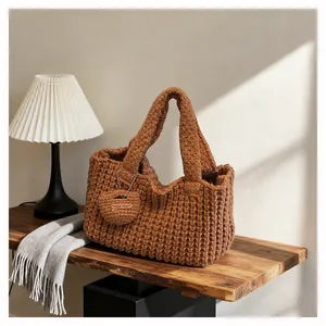 Detail of a brown chunky knit handbag with a handmade heart charm on a wooden table